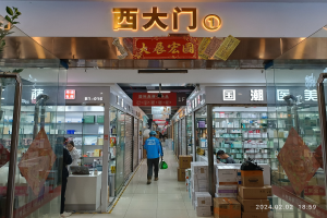 Innenansicht einer chinesischen Apotheke mit Glaswänden, Regalen voller Artikel, verstreuten Kartons, einer Pflanze auf der linken Seite und einem Namensschild oben, das auf eine chinesische Drogerie hinweist.