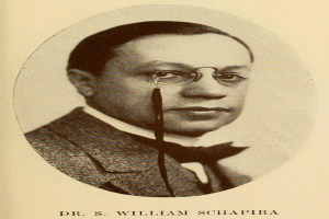 Ein Schwarz-Weiß-Foto von Dr. S. William Schapira in einem Blazer mit Brille, mit Text am unteren Bildrand.