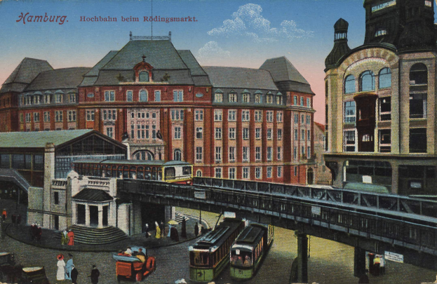 Eine alte Postkarte, die einen Bahnhof in Hamburg, Deutschland, mit Menschen, Fahrzeugen, Gebäuden, einer Brücke und einem bewölkten Himmel zeigt, zusammen mit Text oben.