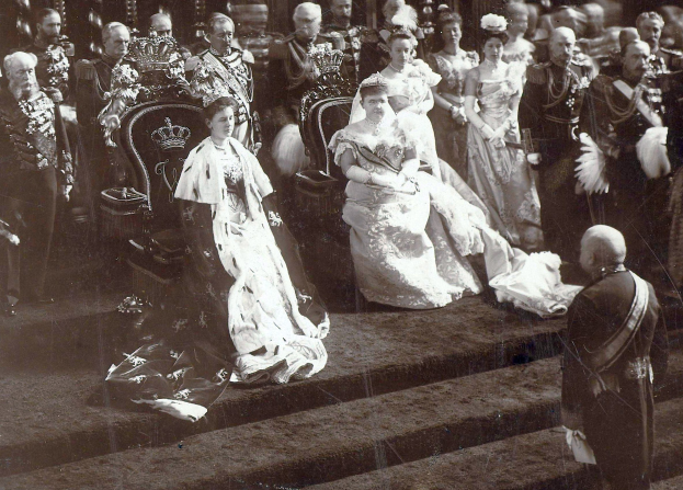 Schwarzes und weißes Foto von Queen Victoria und Prinz Philip, Duke of Edinburgh, sitzend in weißer Hochzeitskleidung mit einigen Menschen im Hintergrund auf einer Treppe stehend.