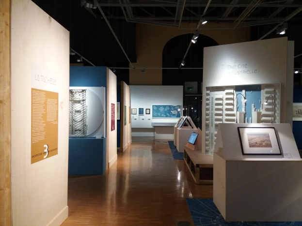 Ein Raum mit verschiedenen Kunstwerken im Museum of Modern Art, darunter gerahmte Fotos auf Tischen, Texttafeln an den Wänden, Deckenbeleuchtung und ein Teppichboden.
