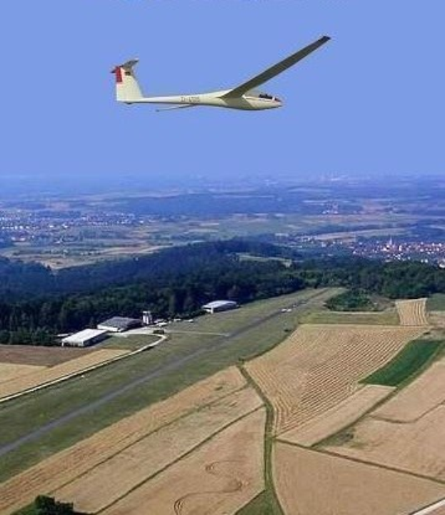 Ein Segelflugzeug, das über einem Feld mit Bäumen und Gebäuden im Hintergrund fliegt, mit Text oben im Bild.