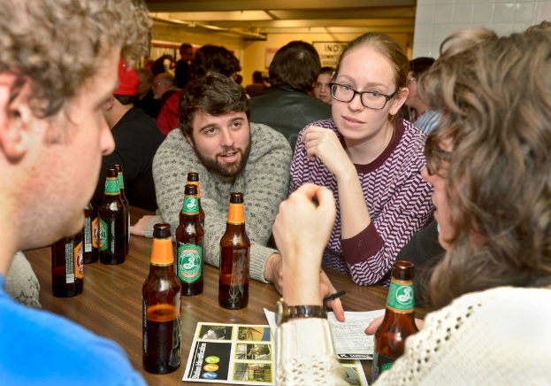 Mehrere Personen auf beiden Seiten eines Tisches mit Bierflaschen in einer Bar-Situation.