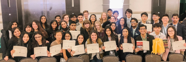 Gruppe von Menschen mit Urkunden bei einer Abschlussfeier sitzend vor einer Wand