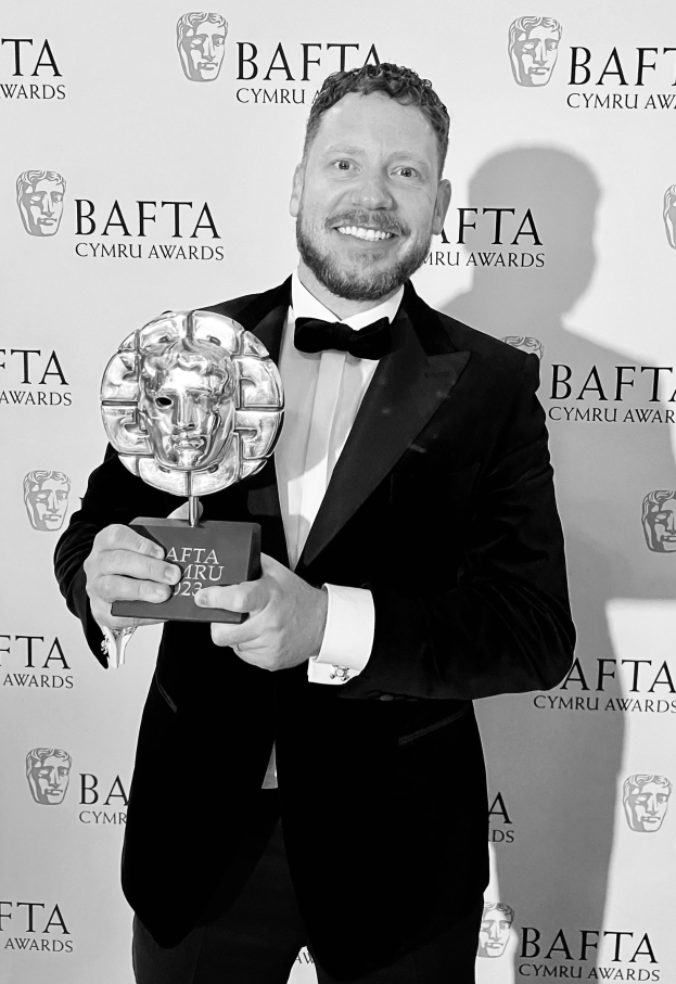 Ein Mann in einem Smoking, der eine BAFTA-Auszeichnung hält und lächelt, mit einem "BAFTA Awards 2018"-Schild im Hintergrund.
