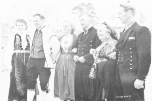 Eine Gruppe von Menschen in den 1930er Jahren, die zusammenstehen, lächeln und von Bäumen im Hintergrund umgeben sind, mit dem Text "Bayerische Familie in den 1930er Jahren" unten.