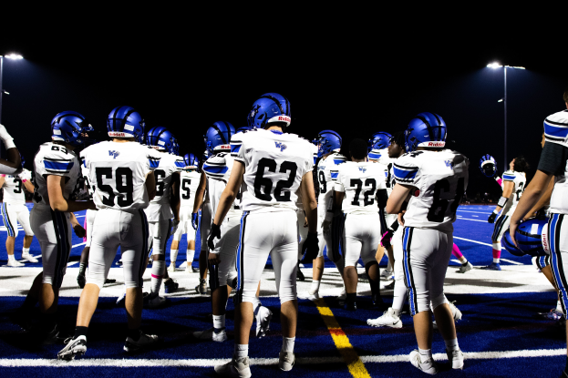 Eine Gruppe von Fußballspielern in Helmen und Stiefeln steht auf einem Feld, mit Leuchten im Hintergrund.
