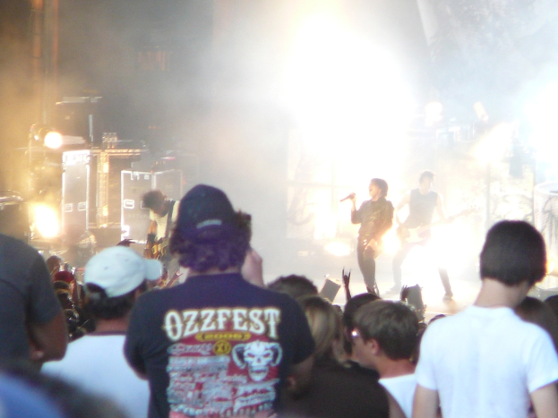 Eine Gruppe von Menschen in verschiedenen Kleidern, einige mit Mützen, in der Nähe von Musikinstrumenten wie einer Gitarre und einem Mikrofon, mit Bühnenbeleuchtung.