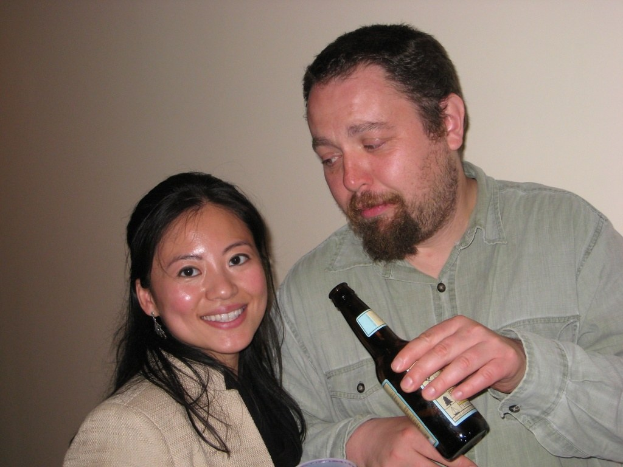 Ein Mann mit einer Flasche schaut eine lachende Frau an einer Wand an.