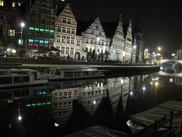 Zwei weiße Boote liegen an einem kleinen Wasserteich, mit Burggebäuden und Straßenlaternen dahinter und einer alten Brücke im Hintergrund.