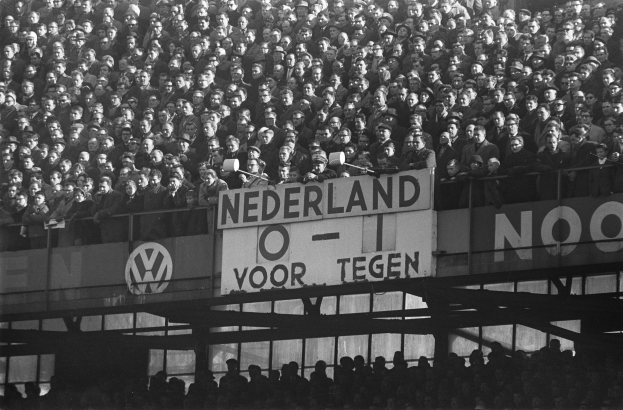 Ein Schwarz-Weiß-Foto einer großen Menschenmenge in einem Stadion, mit einer Tafel in der Mitte und ein paar Individuen unten.