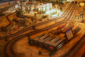 Eine detaillierte Modellbahnausstellung in einem Museum, die Gebäude, Bäume, Schienen, Fahrzeuge und andere Miniaturstädtelemente zeigt, die eine belebte Stadtlandschaft nachahmen.