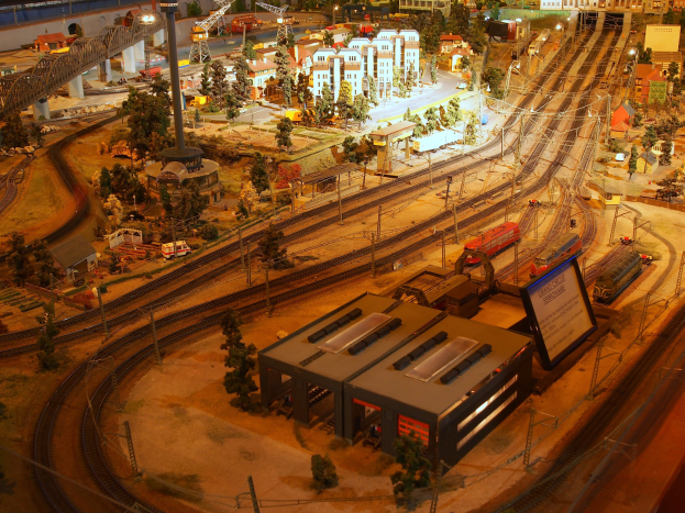 Eine detaillierte Modellbahnausstellung in einem Museum, die Gebäude, Bäume, Schienen, Fahrzeuge und andere Miniaturstädtelemente zeigt, die eine belebte Stadtlandschaft nachahmen.