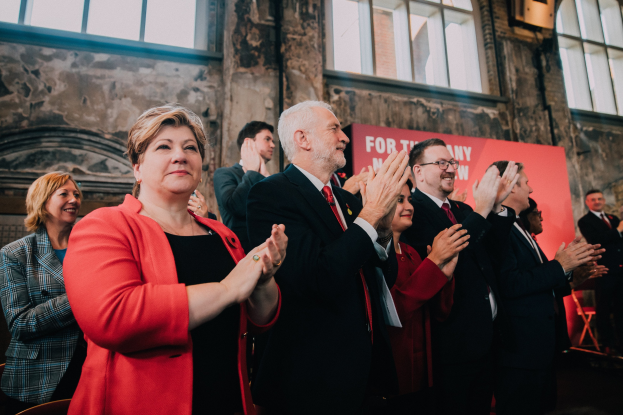 Eine Gruppe von Menschen, die vor einer Menge klatschen und mit einem Banner feiern, das "Wahlsieg" auf einem Gebäude mit Fenstern im Hintergrund trägt.