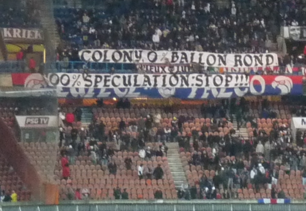 Ein Stadion voller Menschen, Banner und Stühle, mit einem Zaun unten und Treppen auf der linken Seite.