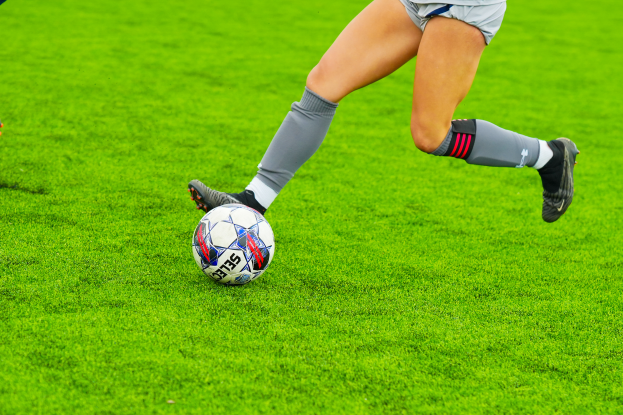 Eine Frau in einem Sportdress kickt einen Fußball auf einem saftig grünen Feld.