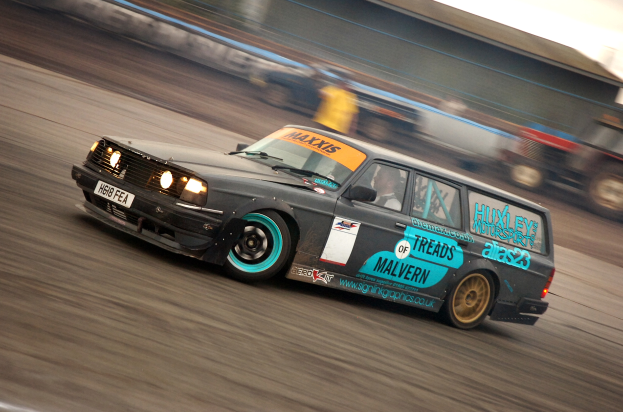 Ein Auto fährt eine Rennstrecke entlang mit einem Fahrer darin, umgeben von anderen Fahrzeugen, mit einem unscharfen Hintergrund, der auf hohe Geschwindigkeit hinweist.
