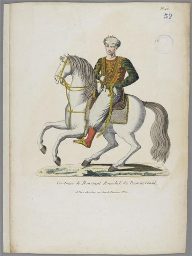 Ein Mann in einem farbenfrohen, detailreichen Manelak-Kostüm reitet auf einem weißen Pferd, das mit Sattel und Zaumzeug geschmückt ist, mit sichtbarem Text, der das Kostüm beschreibt.