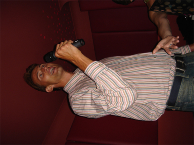 Ein Mann hält ein Mikrofon und spricht, mit einer Wand im Hintergrund.