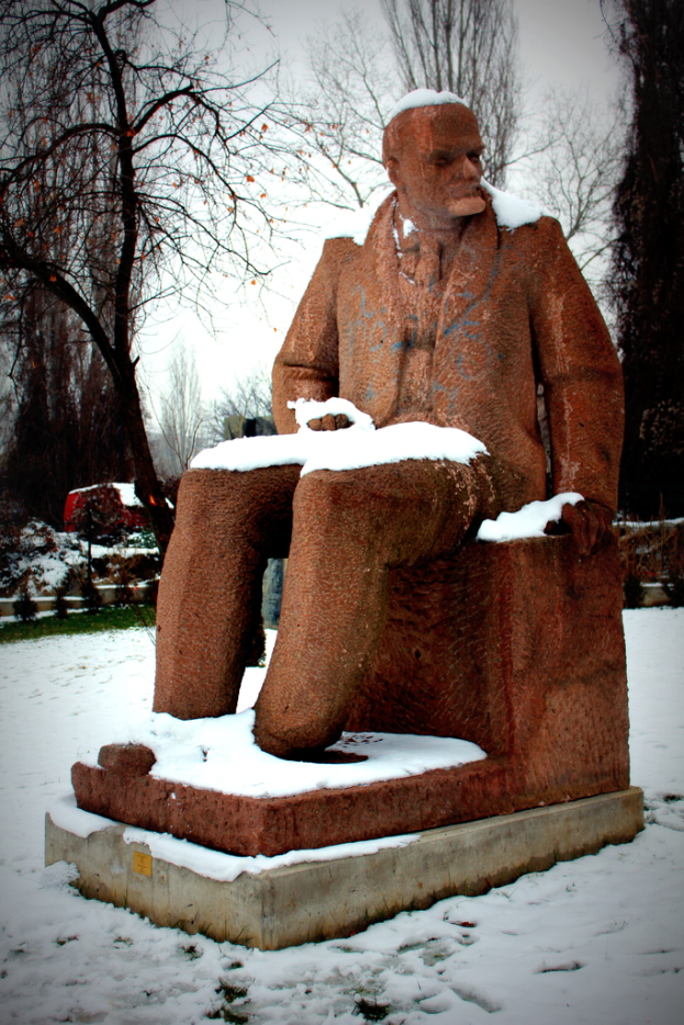 Eine Skulptur einer sitzenden Person umgeben von Schnee mit Bäumen im Hintergrund.