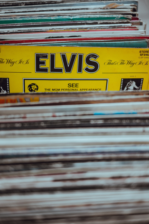Ein ordentlich gestapelter Stapel Elvis-Presley-Platten auf einem Tisch, mit einigen Titeln und einem leicht unscharfen, träumerischen Hintergrund.