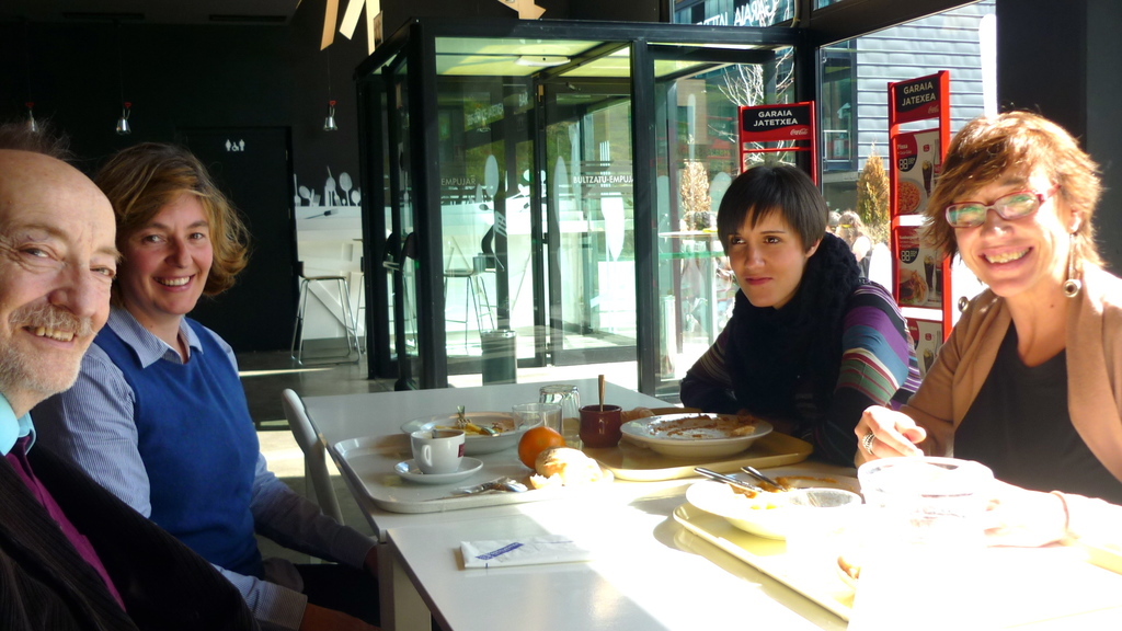 Eine Gruppe von Menschen sitzt an einem Tisch mit Lebensmitteln, mit einer Glastür in der Mitte, wahrscheinlich in einem Hotel.