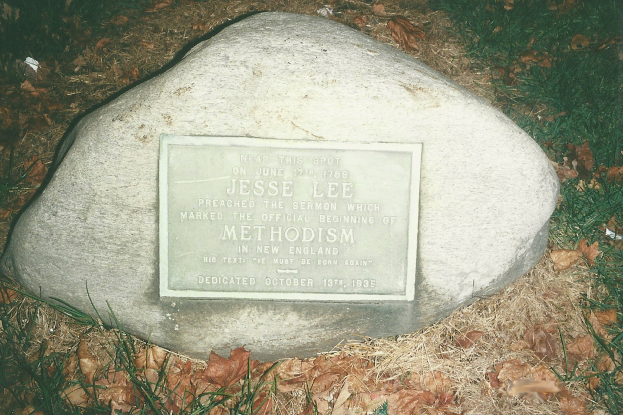 Ein großer Felsen mit einer Tafel, auf der "Jesse Lee Methodism" steht, in einem grasigen Bereich umgeben von trockenen Blättern und Gras.
