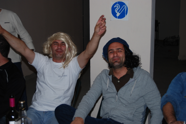 Eine Gruppe von Menschen sitzt auf Stühlen mit Flaschen auf einem Tisch vor ihnen und einem Schild an der Wand dahinter.