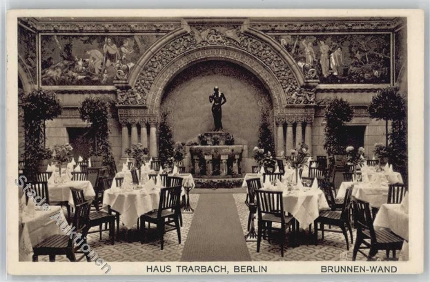 Schwarzes und weißes Foto eines alten Berliner Restaurantinnenraums mit Tischen, die mit Vasen und Skulpturen auf den Wänden, einer Statue im Hintergrund und Text am unteren Rand dekoriert sind.
