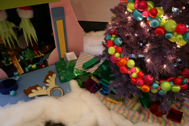 Drinnen, ein geschm├╝ckter Weihnachtsbaum rechts, Geschenkboxen und Deko in der Mitte, eine H├╝tte mit Deko ├╝ber links und Baumwolle und Wolle unten.