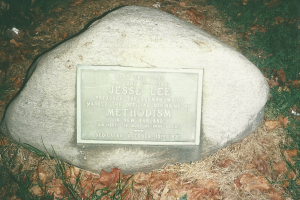 Ein großer Felsen mit einer Tafel, auf der "Jesse Lee Methodism" steht, in einem grasigen Bereich umgeben von trockenen Blättern und Gras.