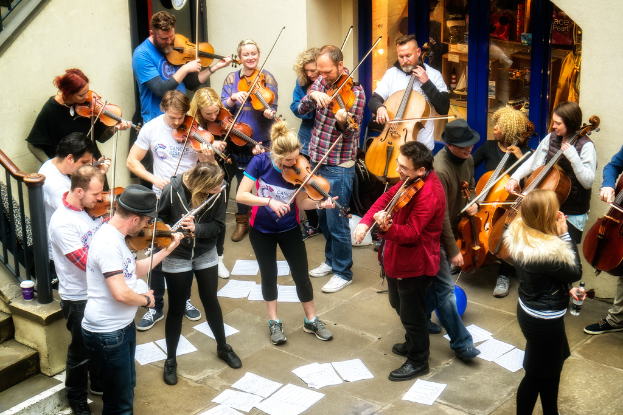 Eine Gruppe von Menschen spielt Geigen mit verstreuten Papieren auf dem Boden.