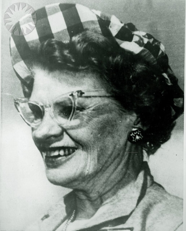 Eine Frau mit Brille und einem weißen und schwarzen Hut lacht.