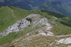 Gruppe von Menschen beim Wandern auf einem Berg mit grünem Gras und steinigem Gelände, der Himmel ist im Hintergrund sichtbar.