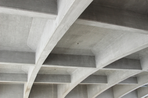 Nahaufnahme einer Betonstruktur mit mehreren Balken und einem Gebäude in der unteren rechten Ecke.