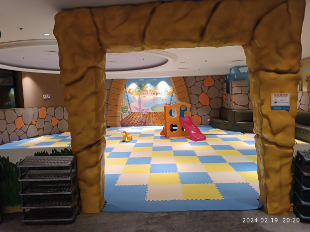 Kinderspielbereich mit einem zentralen Torbogen, verstreuten Spielzeugen auf dem Boden, Regalen auf beiden Seiten, einer bemalten Wand im Hintergrund und Deckenbeleuchtung.