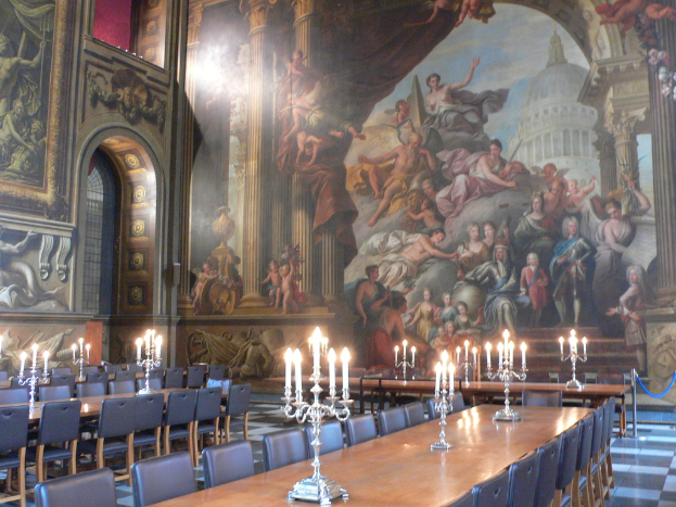 Ein Raum mit Tischen und Stühlen, Kerzen auf Ständern, eine Wand mit einem Bogen und Gemälde an der Wand.