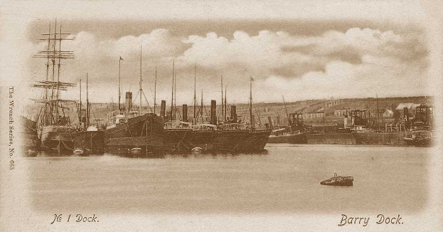 Ein Schwarz-Weiß-Foto von Booten, die am Barry Dock in Wrexham, England, liegen, mit Gebäuden im Hintergrund und Wolken am Himmel.