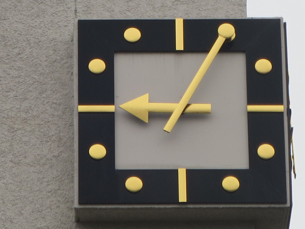 Uhr an der Seite eines Gebäudes mit weißem Hintergrund, die Zeit über Stunden- und Minutenzeiger anzeigt.