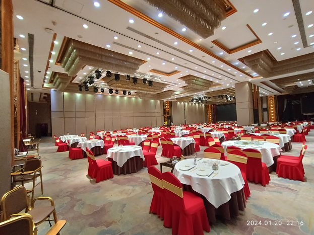 Großer Ballsaal mit weißen Tischdecken, Gläsern, Tellern, Besteck und Dekoration an den Wänden sowie beleuchteter Decke, mit Wasserzeichen unten rechts.