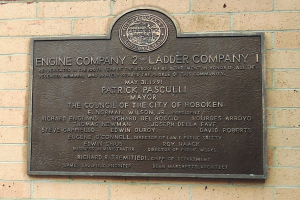 Schwarzes rechteckiges Schild mit weißer 'Engine Company 2 Ladder Company'-Aufschrift an einem Backsteingebäude.