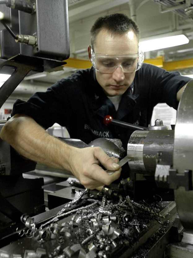 Ein Monteur mit Brille bedient eine Maschine in einer hell erleuchteten Fabrikumgebung.