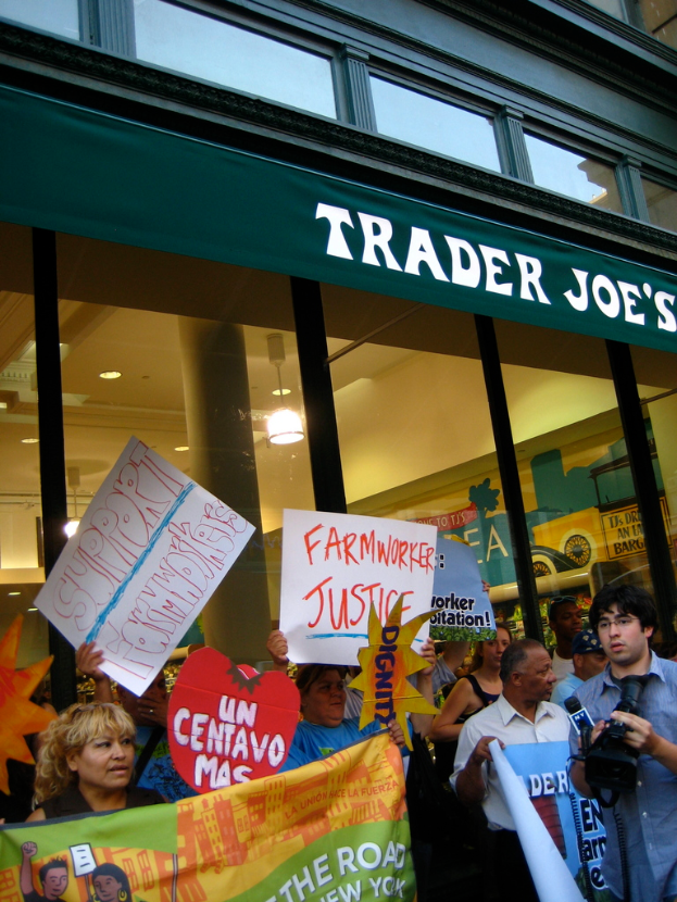Eine Gruppe von Menschen, die vor einem Geschäft stehen und Schilder und Plakate halten, mit einer Säule und Lichtern auf dem Dach im Hintergrund.
