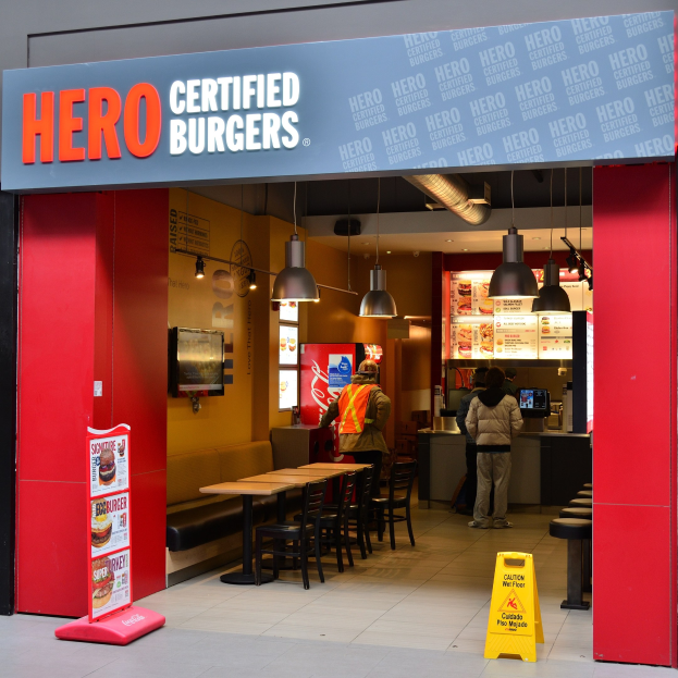 Ein Hero Certified Burgers Restaurant im Innern von London mit Gästen, Tischen, Stühlen, einer Speisekarte, einem wandmontierten Fernseher und Deckenleuchten.
