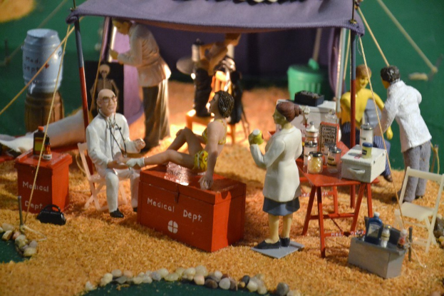 Eine Sammlung von Spielzeugen, einschließlich einer auf einer Schachtel mit der Aufschrift "medizinisches Departement", mit einem Tisch, der Gegenstände in der rechten Ecke hält, unter einem violetten Zelt und zusätzlichen Gegenständen im Hintergrund.