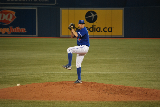 Ein Spieler steht auf dem Boden und hält einen Ball in der Hand, im Hintergrund ein großes Banner mit Text und Bildern.