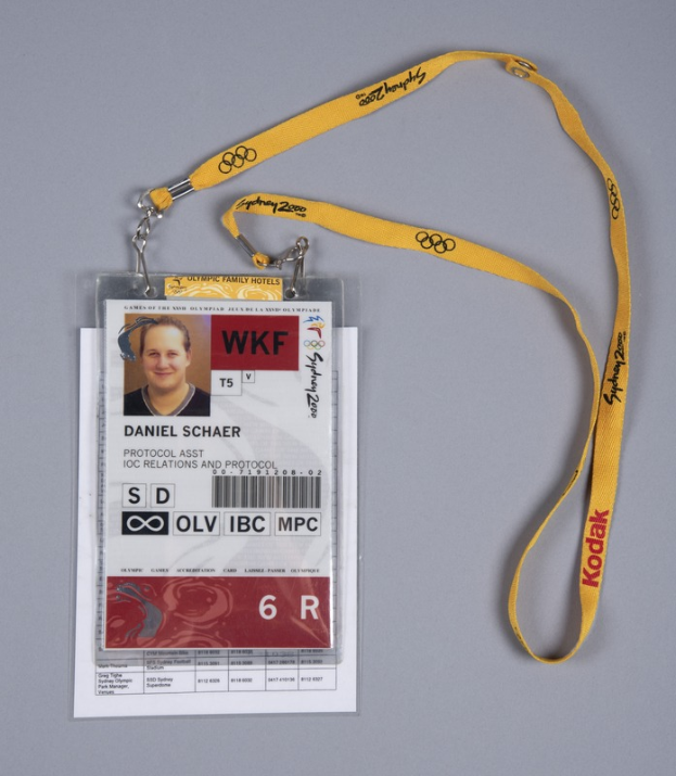 Ein ID-Karte mit einem Foto und Text, an einem gelben Band befestigt, liegt auf einer Oberfläche.