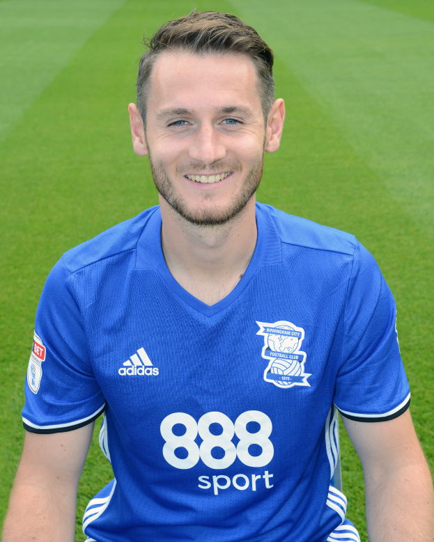 Ein Mann sitzt auf einem Fussballfeld in einem blauen T-Shirt, lächelt und hat einen Trainings-Session-Text unten.