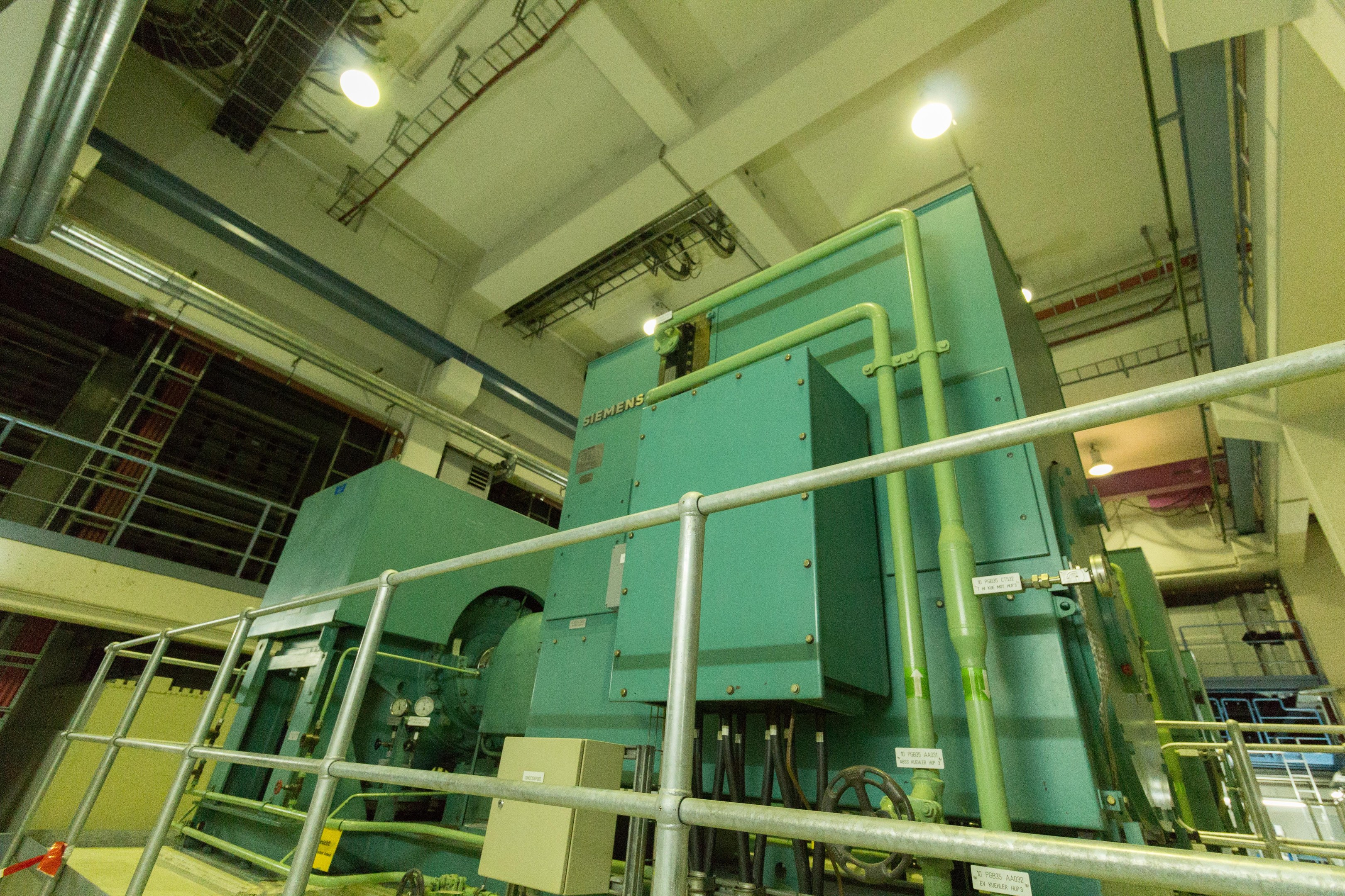 Großer industrieller Wärmetauscher in einem Gebäude umgeben von Geländern, Rohren, Ventilen und Beleuchtungssystemen.