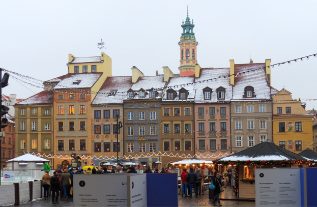 Ein lebendiger Weihnachtsmarkt im alten Stadtzentrum von Warschau mit Menschen um geschmückte Buden, Gebäuden mit Fenstern im Hintergrund und einem Verkehrsampelmast auf der linken Seite.